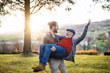 Young man carrying his senior father in arms in nature, having fun.