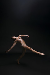 Naked graceful man dancing against black background