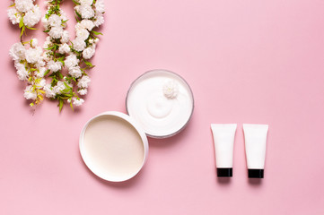 Obraz na płótnie Canvas Beauty Spa concept. Opened plastic container with cream, cosmetic bottle containers, spring White flowers on pink background Flat lay top view. Herbal dermatology cosmetic hygienic cream organic