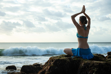Fototapeta na wymiar Young woman meditating, practicing yoga and pranayama with namaste mudra at the beach, Bali