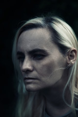 Portrait of blonde woman in a dark, creepy feel, with dark shadows hiding her eyes, negative emotions, horror 