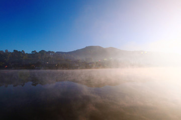 Fototapeta na wymiar Beautiful landscape heaven of mist and fog over the lake and sunrise shining with blue sky reflection on the water surface at Hill tribe village on mountain in Thailand