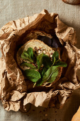 In a paper bag, slices of fresh bread, basil leaves and sprinkled grain. Fabric background.