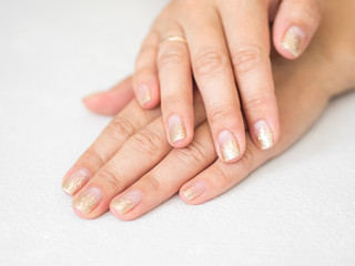 Fototapeta premium Manicure salon concept. Beautiful women hands with golden nail manicure on a white background. Gold nail polish. Closeup