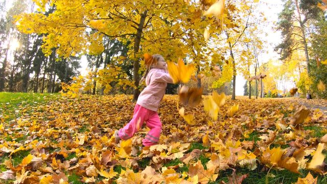 little laughing pretty girl wearing pink raincoat throwing yellow leaves in autumn park