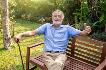 Happy senior old caucasian man holding cane sitting on bench in garden