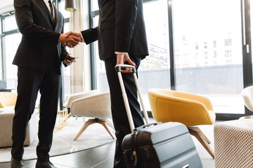 Colleagues indoors in business center office using mobile phone shaking hands.