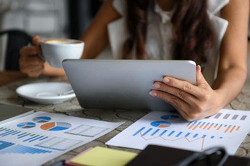 Female executive drink coffee and use tablet during break.She sat by the window in the office.Data graph placed on the desk.