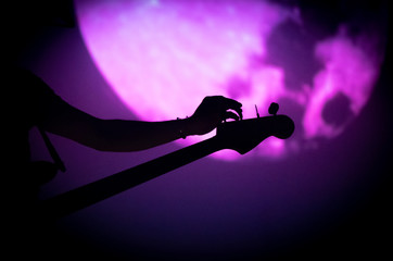 Silhouette of bass guitarist's tuning his instrument during concert with black and purple background