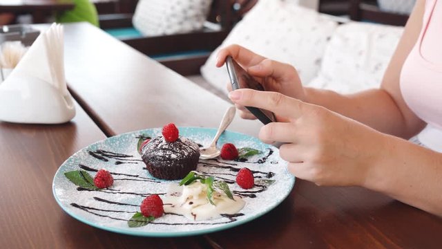 Food blogger hands using smartphone taking photo of beautiful muffin with ice cream on blue plate inside the cafe to share on social media. Top view food photo. Lifistyle concept.