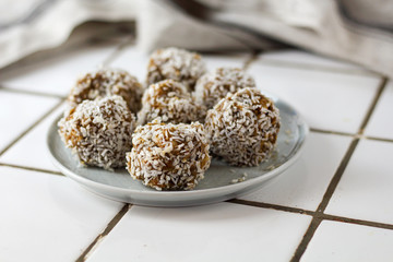 vegetarian raw healthy diet  no bake candies balls dessert sweets sugar free gluten-free with coconut flakes, proper nutrition snack on blue plate on a white tile background, soft selective focus