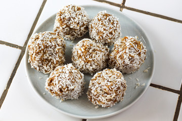 vegetarian raw healthy diet  no bake candies balls dessert sweets sugar free gluten-free with coconut flakes, proper nutrition snack on blue plate on a white tile background, soft selective focus