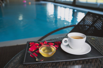 a Cup of tea with rose petals and a vase of honey on the background of the pool