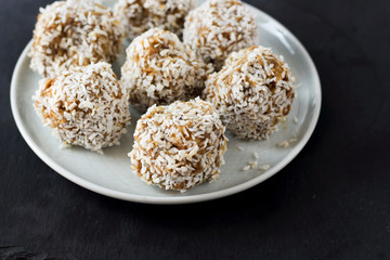 vegetarian raw healthy diet  no bake candies balls dessert sweets sugar free gluten-free with coconut flakes, proper nutrition snack on blue plate and black slate background, soft selective focus