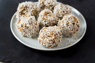 vegetarian raw healthy diet  no bake candies balls dessert sweets sugar free gluten-free with coconut flakes, proper nutrition snack on blue plate and black slate background, soft selective focus