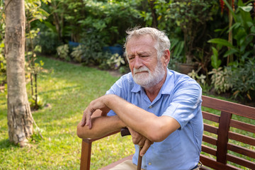 Thoughtful senior old caucasian man holding cane sitting on bench in garden