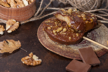 Slices of apples in chocolate, caramel glaze and walnuts on skewers on a dark background