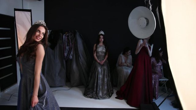 girl model, brunette, in a gray long dress with a deep neckline, beautiful hair and bright makeup, with a crown on her head, posing in the Studio, on a black background, flash, slow motion