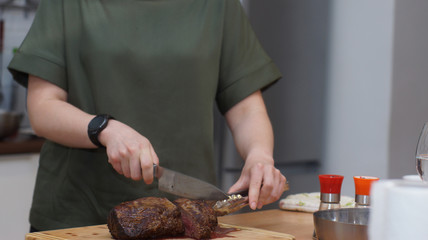 A cook with a round clock slices a baked beef tenderloin on a wooden board