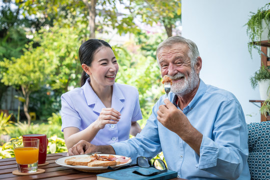 Nurse assist elderly senior man to eat breakfast at nursing home