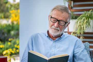 Senior elderly man wearing glasses reading book in garden