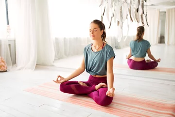 Tuinposter mindfulness, spirituality and healthy lifestyle concept - woman meditating in lotus pose at yoga studio © Syda Productions