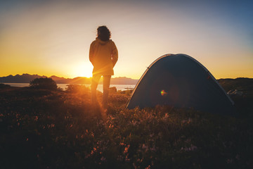 Traveler girl in a yellow jacket stands next to a tent in Norway at sunset
