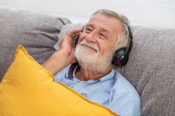 Senior old man eldery enjoy listening to music with headphone on couch sofa
