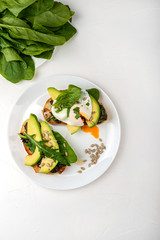 Breakfast. Bread toasts with poached egg and avocado with spinach, fresh arugula and seeds