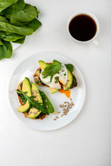 Breakfast. Bread toasts with poached egg and avocado with spinach, fresh arugula and seeds and a cup of coffee