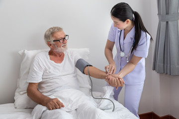 Obraz premium Happy nurse checking and measuring elderly man blood pressure in bedroom at nursing home