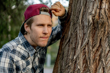 self confident young male teenager looking forward and lean on the tree