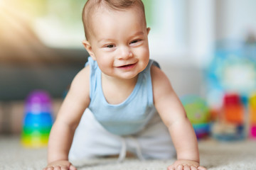 Cute smiling baby boy crawling on floor in living room