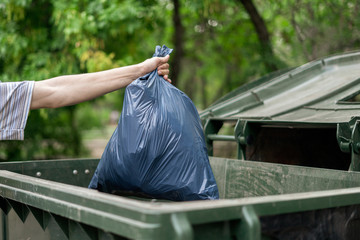 male dumping waste package into a big trash bin container