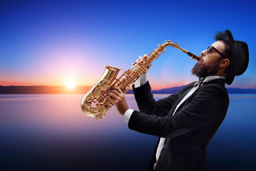 Fototapeta na wymiar Male jazz musician playing a saxophone with a sunset and water