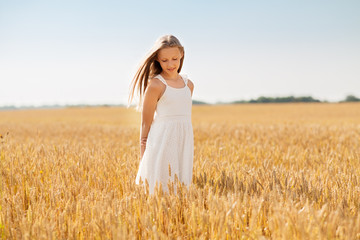 Fototapeta na wymiar nature, harvest and people concept - smiling young girl on cereal field in summer