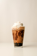 Ice coffee in the glass topped whipping cream with coffee beans. Cold summer drink on wooden background and copy space. Advertising for caramel mocha and chocolate beverage for the cafe.
