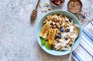 Oatmeal with caramel, banana, blueberries and coconut chips on a concrete background.