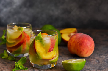Cold lemonade with peach and lime on a dark concrete background.
