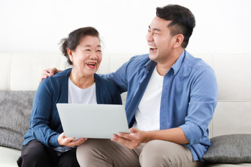 Asian young man and senior woman using laptop computer in living room concept Son teach mother use computer laptop