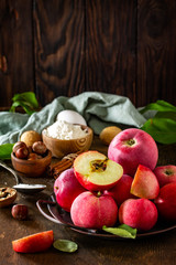 Apple baking seasonal concept. Ingredients for apple pie (red apple, flour, eggs, anise, hazelnut, sugar and cinnamon) on a rustic wooden table. Free space for your text.