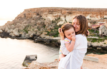 Family of mother and toddler child watch sunset at sea 