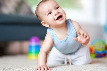 Cute smiling baby boy crawling on floor in living room