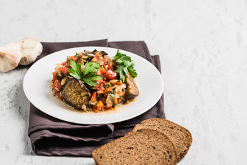 Summer salad of eggplant and tomato on a white plate on a light background