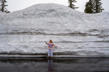 Cute blonde tourist woman poses and stands next to a large mound of plowed snow in Lassen National Park California during summer