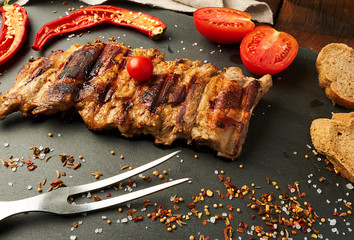grilled pork ribs on a black board, fresh red tomatoes