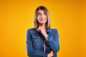 Close up of woman in denim jacket thinking and pointing over yellow background