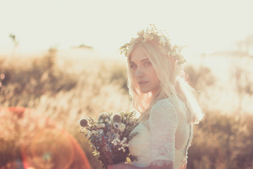 Beautiful young woman portrait in a white dress in boho style with a floral wreath in the summer in the field. Selective soft focus. © Roman