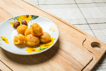 Apricots with bones in small plate on wooden board.