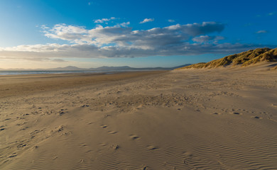 Fototapeta na wymiar Views along the beach with sand dunes and mountains in the distance, Harlech, North Wales